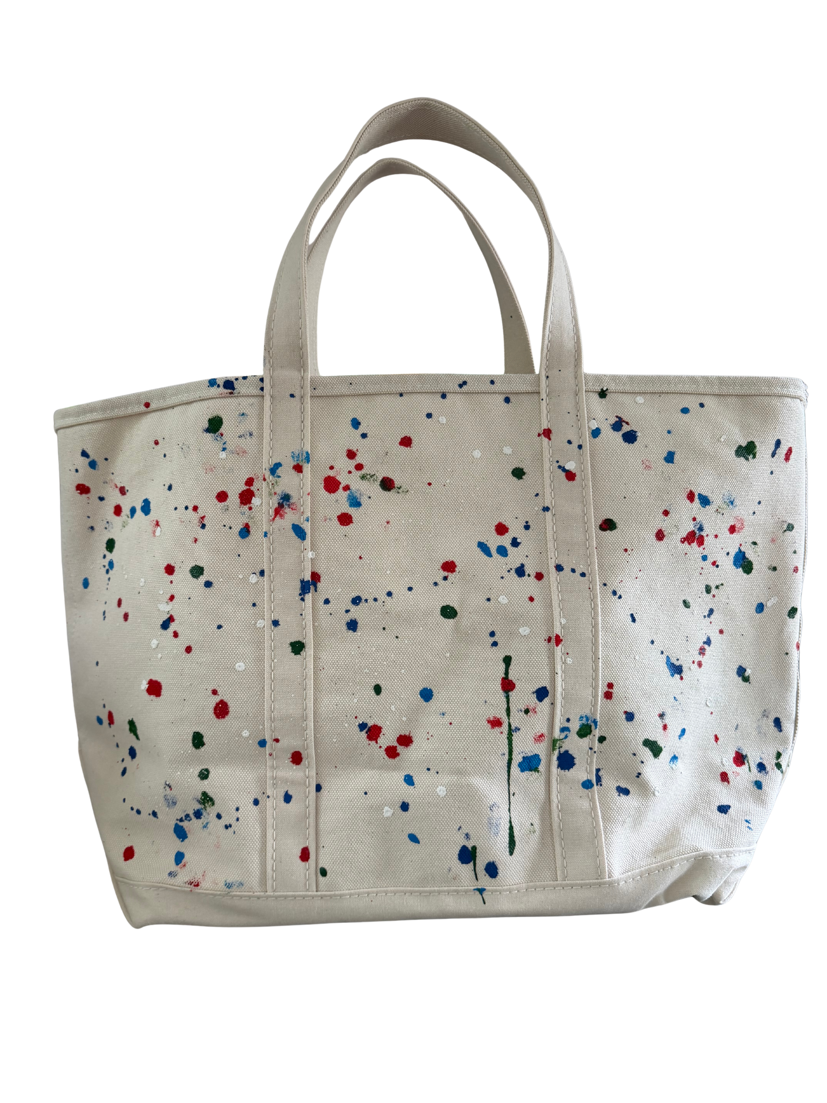 A canvas tote bag in a warm off-white or cream color, decorated with a colorful paint splatter pattern in red, blue, green, and white. The bag features two top handles and is photographed against a solid white background.