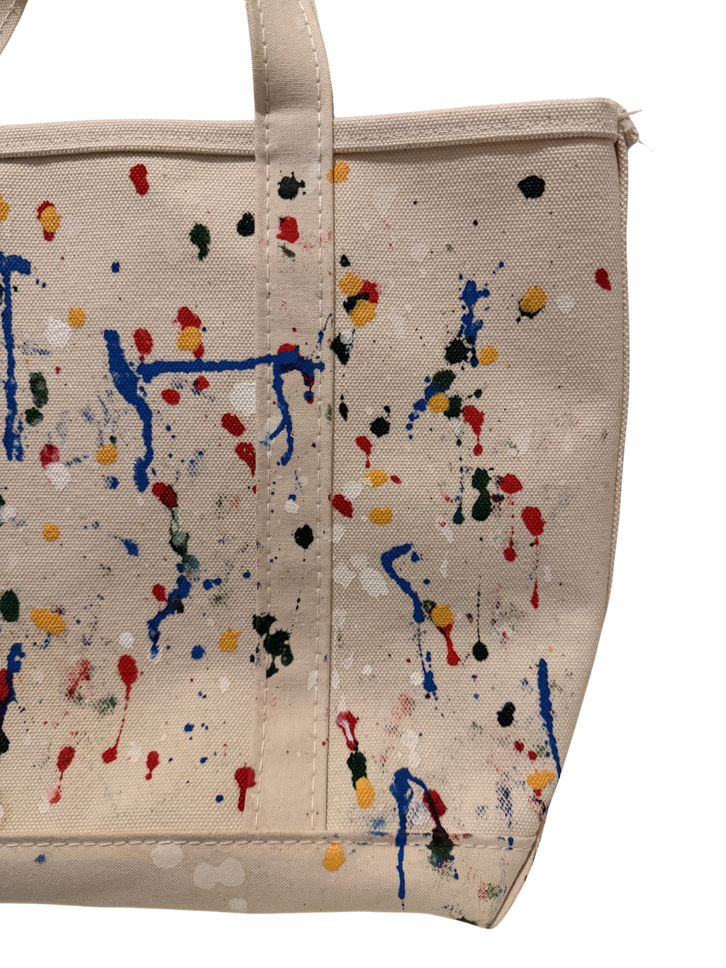 Beige canvas tote bag with a colorful paint splatter and drip pattern in blue, red, yellow, green, and white, shown against a plain white background.