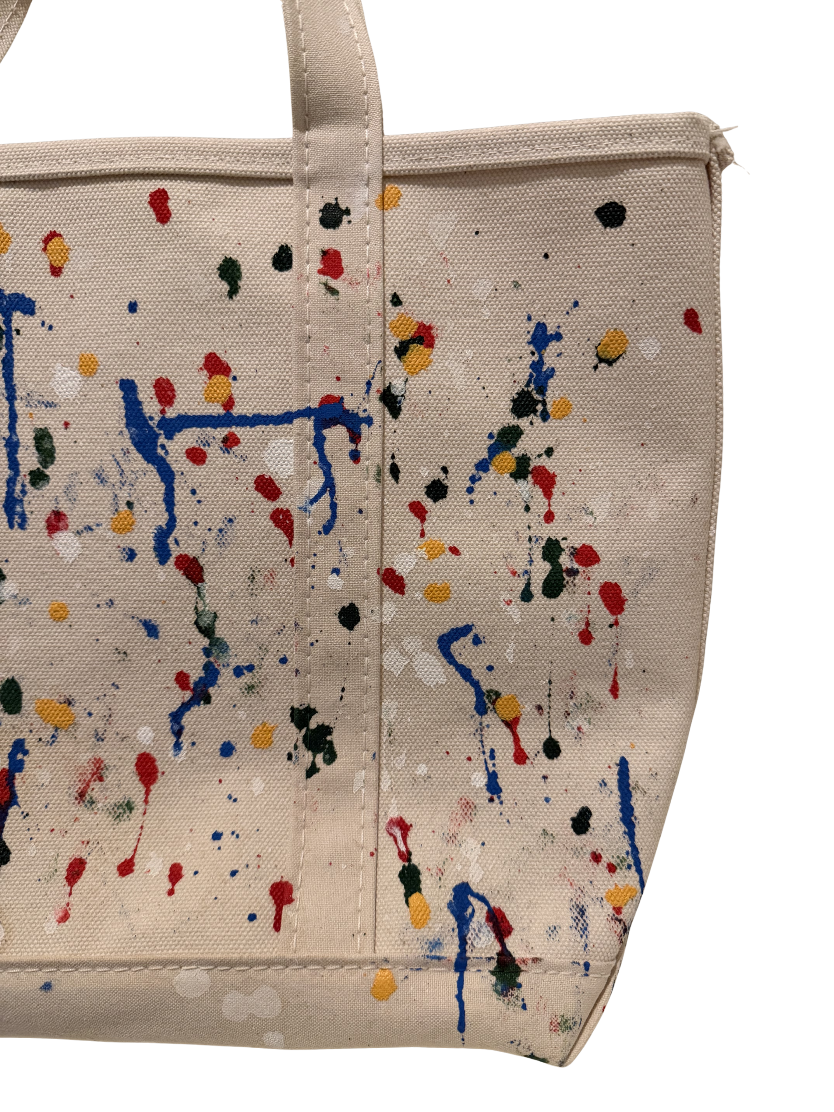 Beige canvas tote bag with a colorful paint splatter and drip pattern in blue, red, yellow, green, and white, shown against a plain white background.