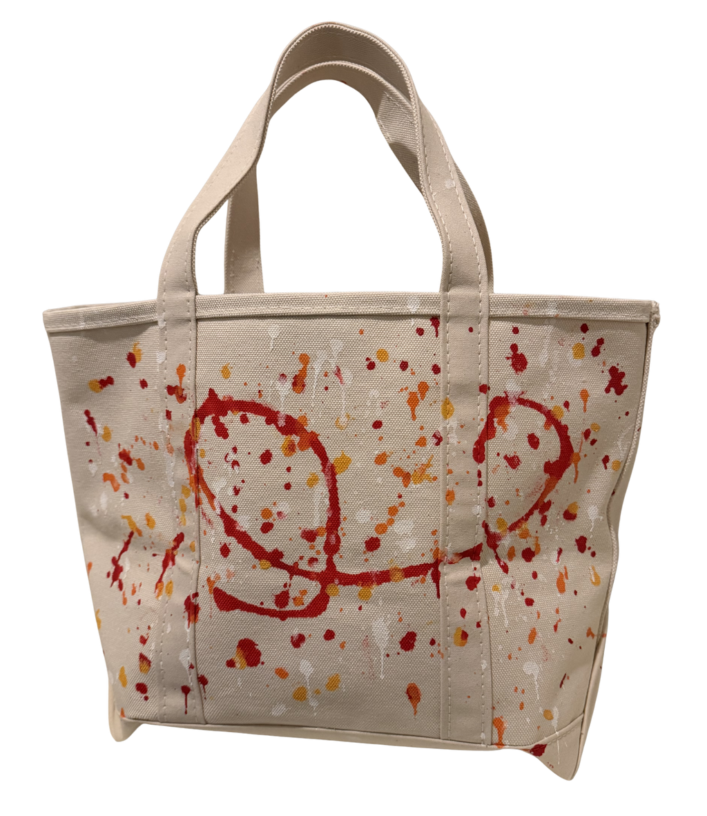 A canvas tote bag in a light beige color, decorated with red and orange paint splatters and abstract red scribbles on the front, set against a plain white background.