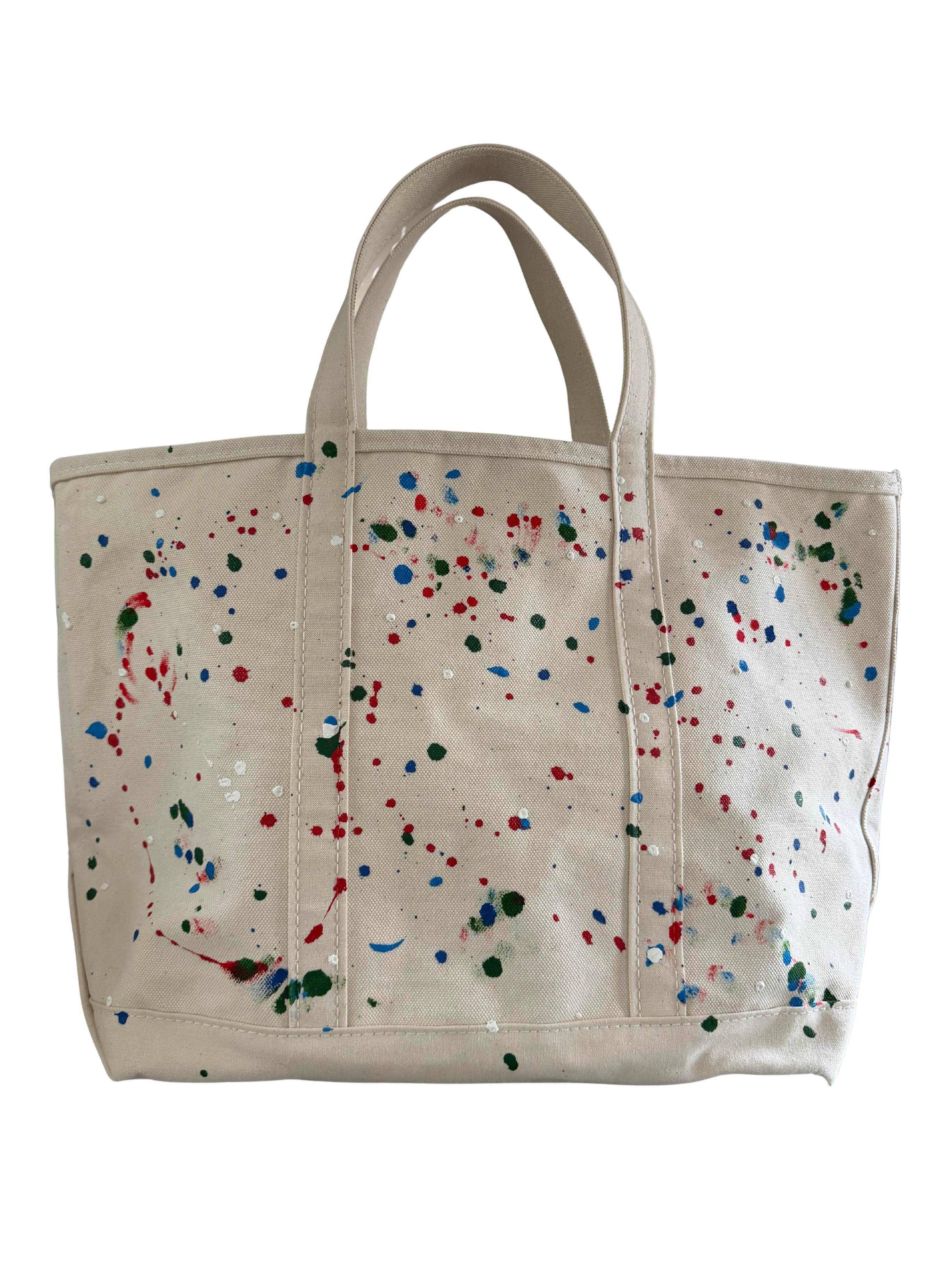 An off-white canvas tote bag with colorful paint splatters in red, blue, green, and white, featuring dual top handles, shown against a plain white background.